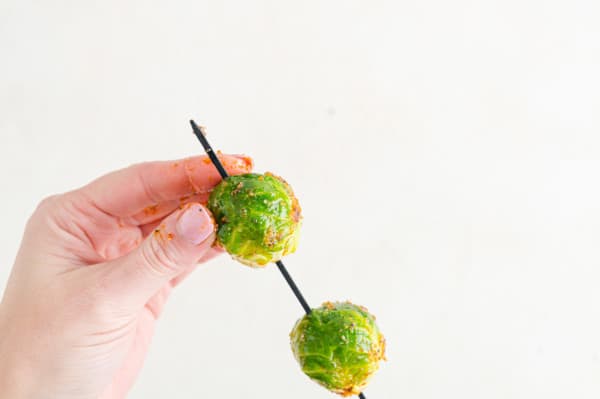 A hand adds seasoned Brussels sprouts onto a skewer.