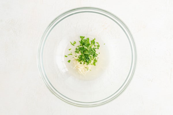 Parmesan, parsley, and lemon juice combined in a glass bowl.