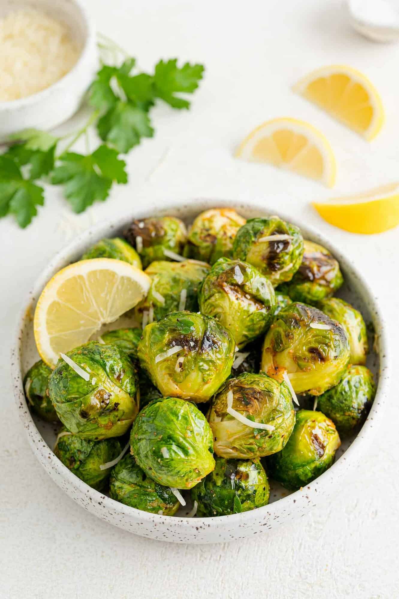 A bowl of grilled Brussels sprouts tossed in lemon and parmesan, garnished with lemon wedges.