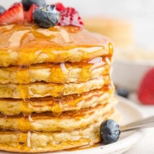 Quinoa pancakes in a stack with berries and maple syrup.