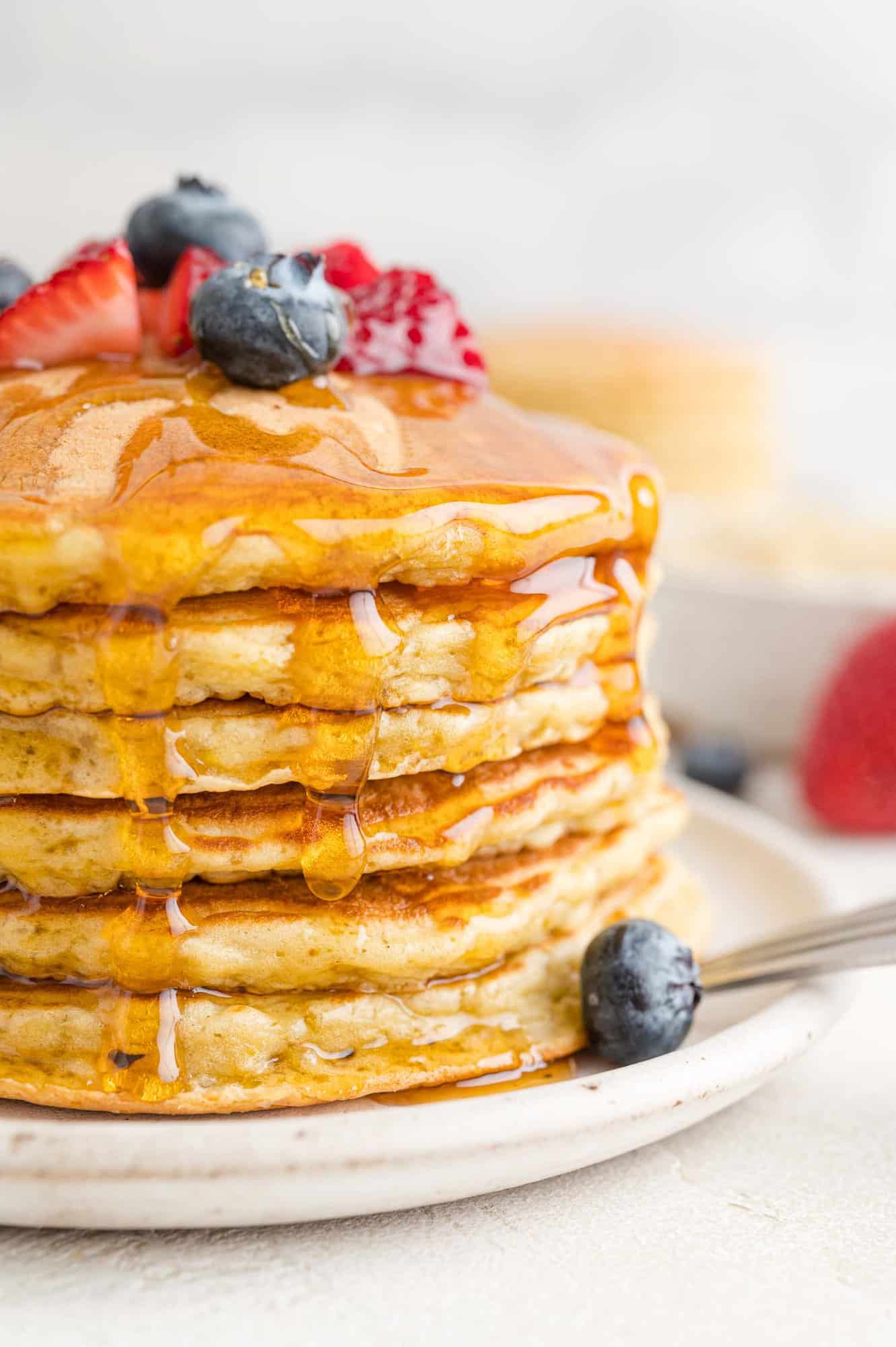 Quinoa pancakes in a stack with berries and maple syrup.