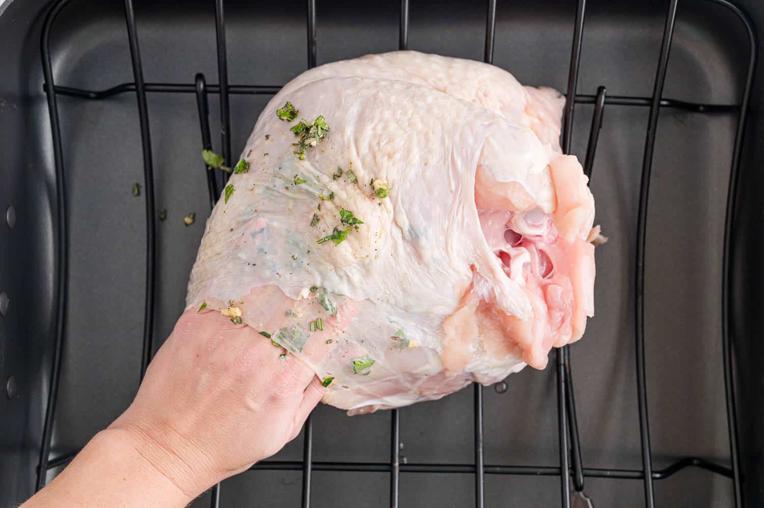 Uncooked turkey breast being rubbed with herbs.