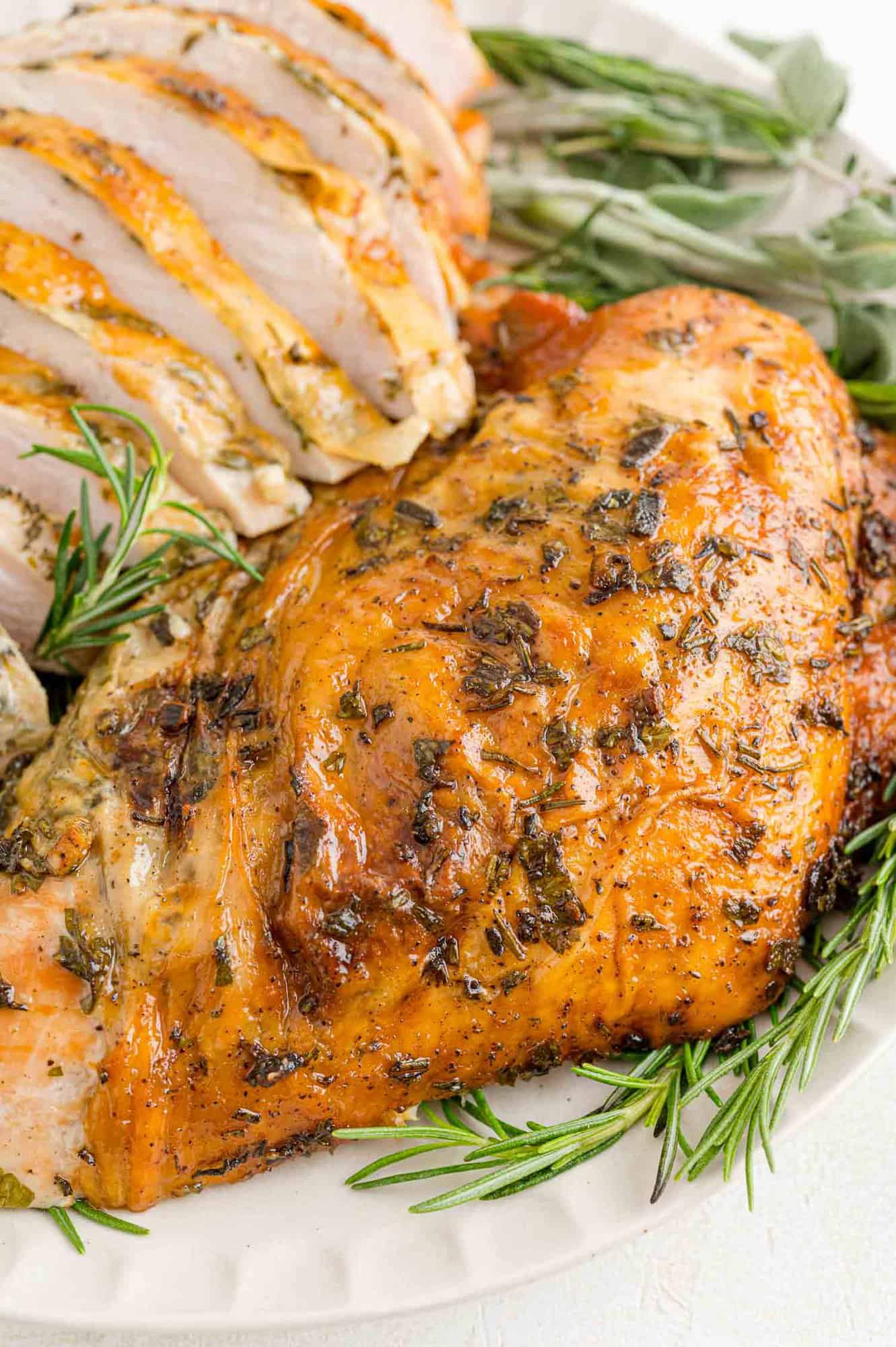 Herb rubbed roasted turkey breast on a platter with fresh herbs.