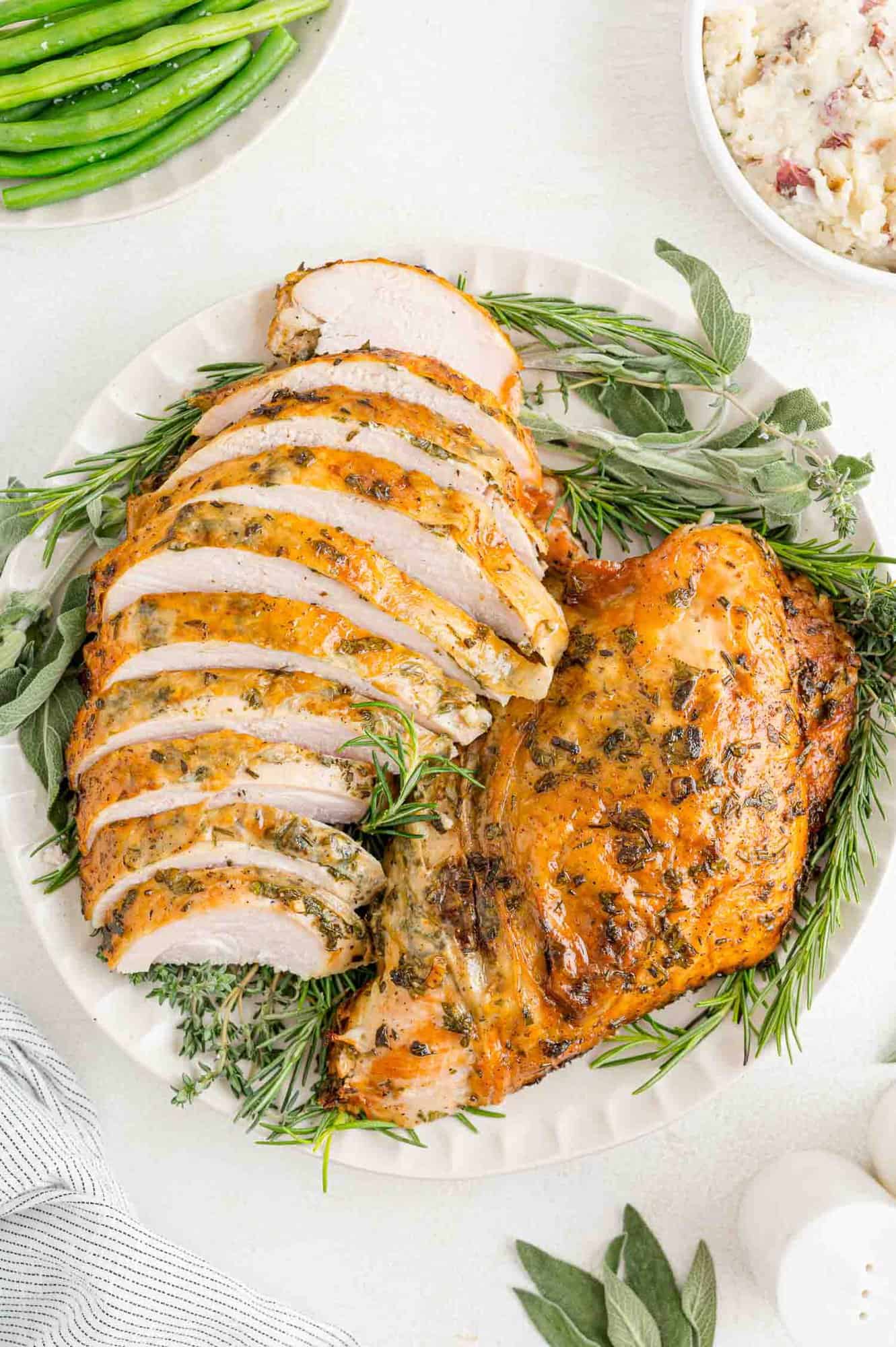 Herb roasted turkey breast on a platter with fresh herbs.