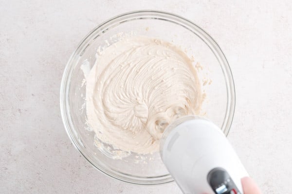 A hand mixer is used to combine the ingredients for fruit dip in a glass bowl.