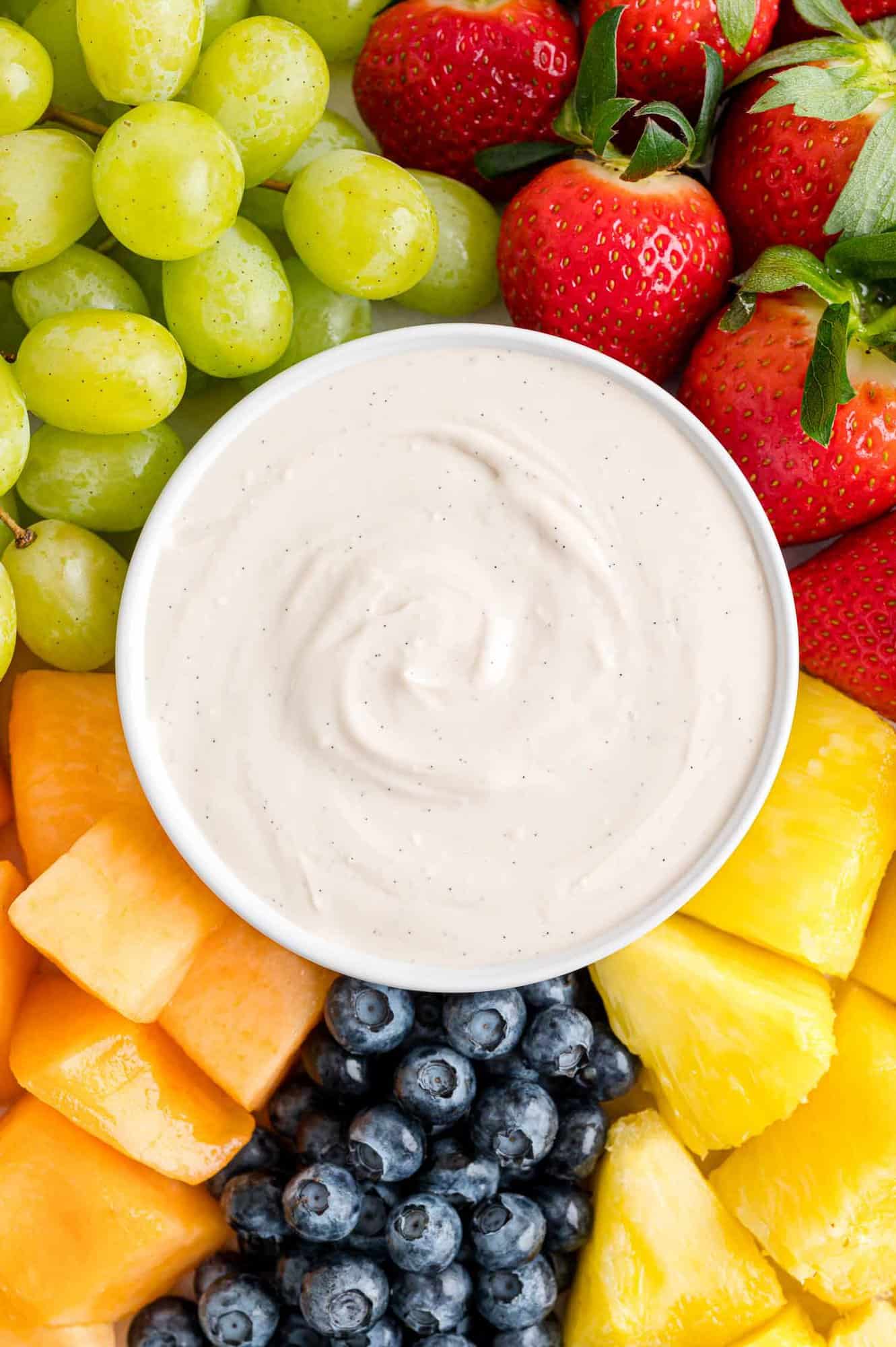 Overhead view of a bowl of cream cheese fruit dip in the center of a fruit platter with assorted fruits and berries.