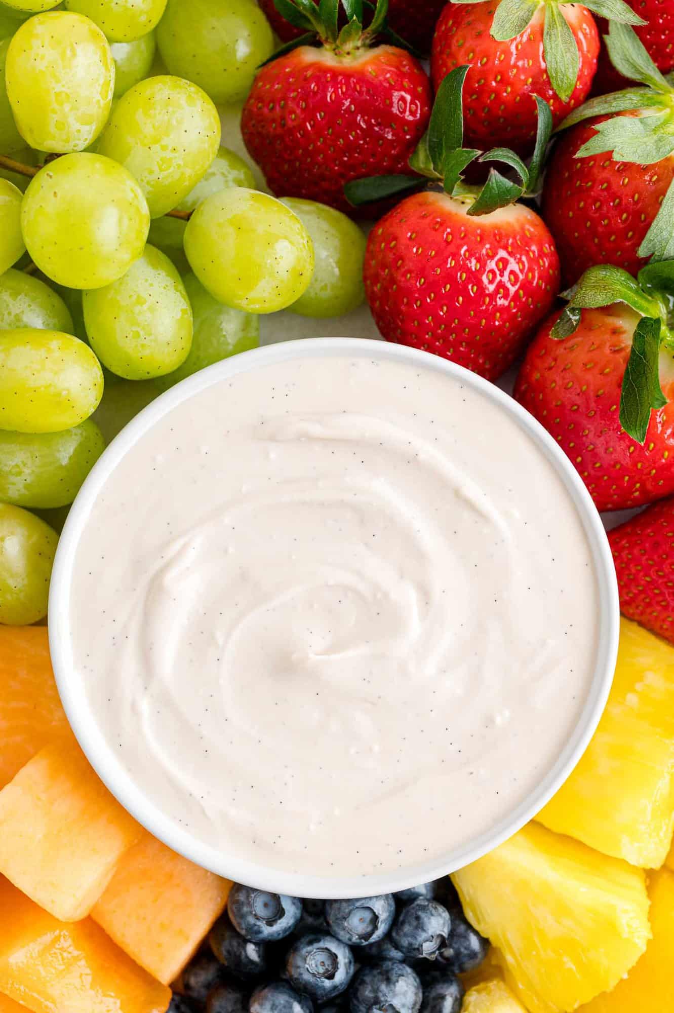 Overhead view of a bowl of cream cheese fruit dip in the center of a fruit platter with assorted fruits and berries.