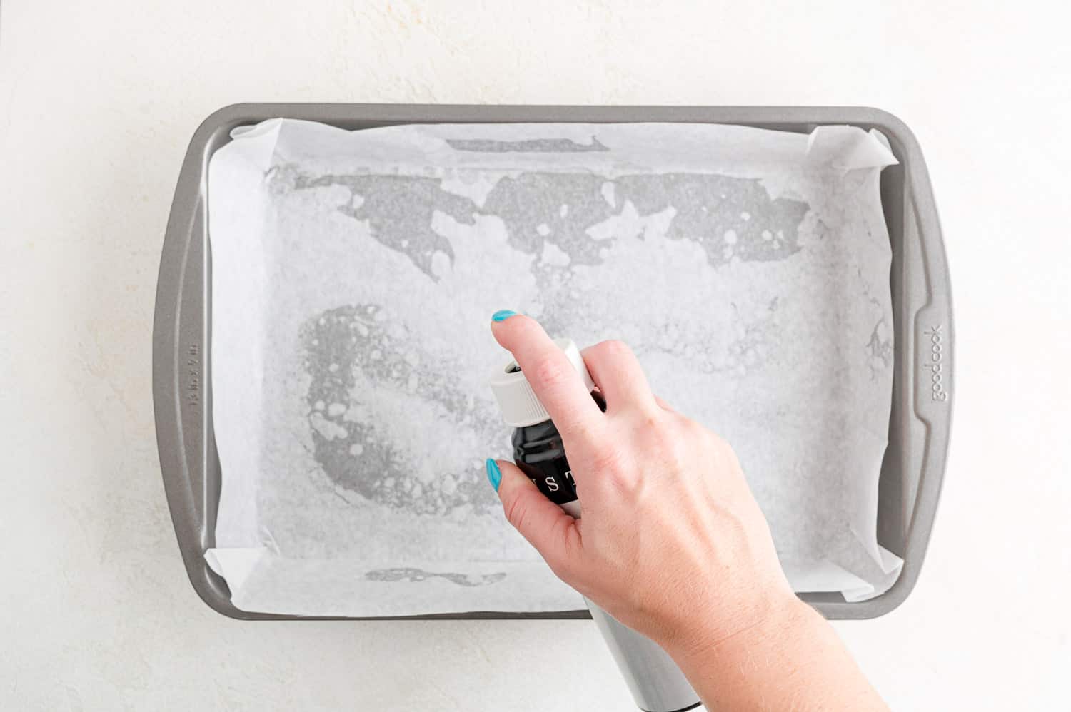 Parchment paper lined baking pan being sprayed with nonstick cooking spray.