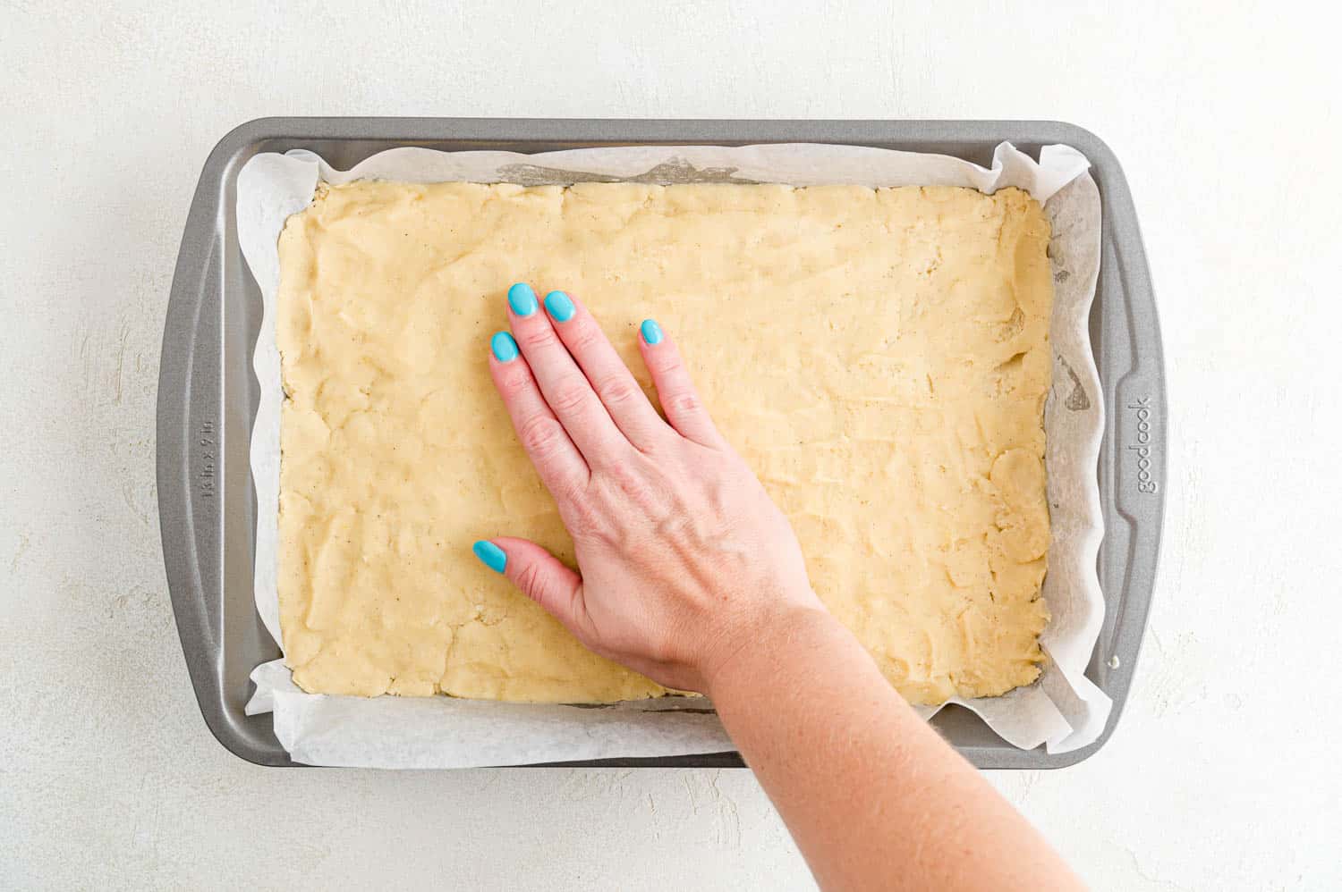 Cookie dough being pressed into pan.