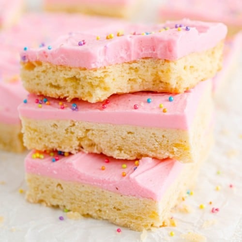 Sugar cookie bars with pink frosting and sprinkles, stacked three high.