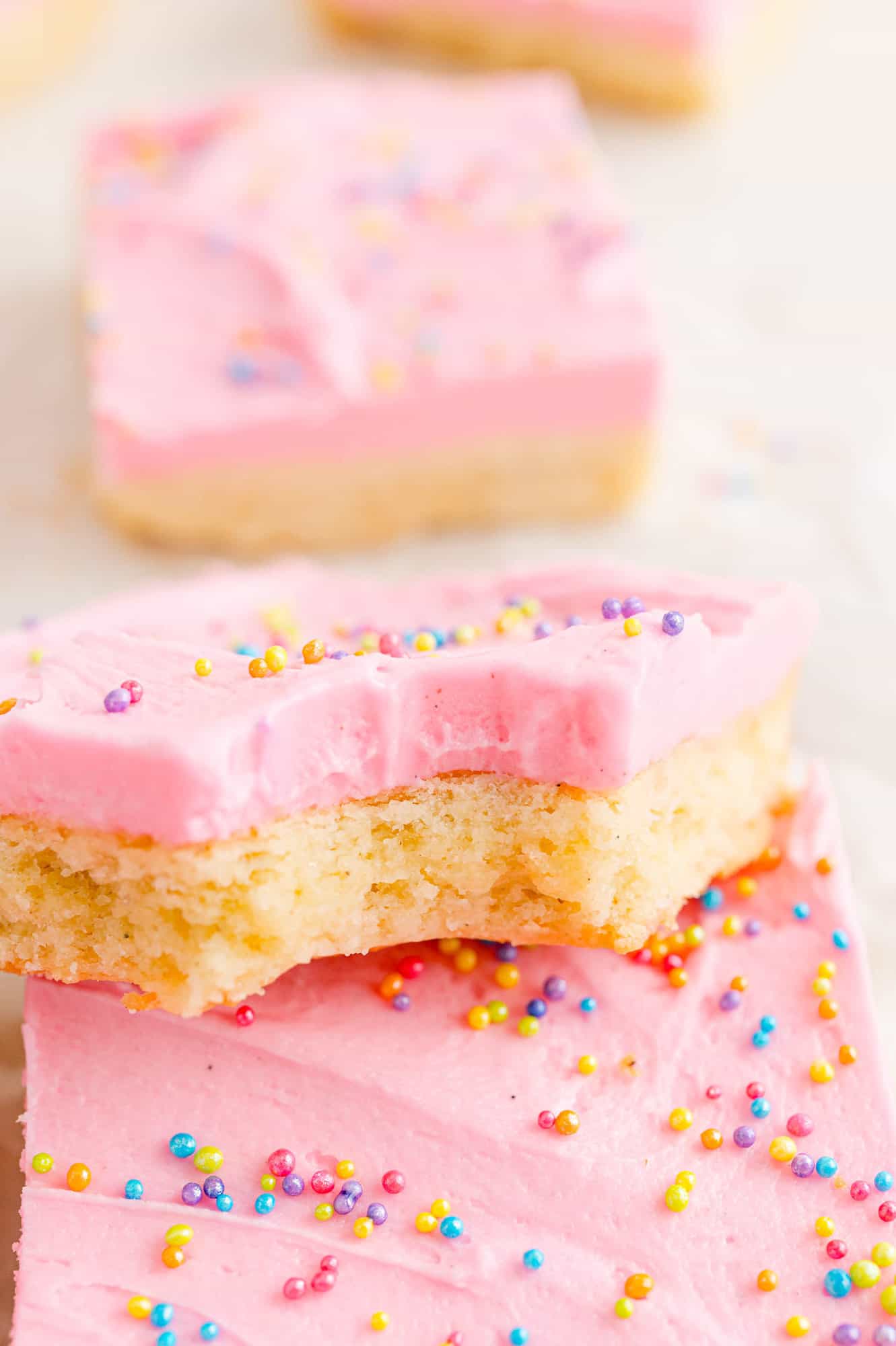 Cookie bar with pink frosting, bite taken out of it to show texture.