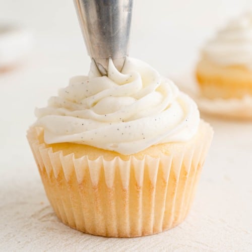 Vanilla buttercream frosting being piped onto a cupcake.