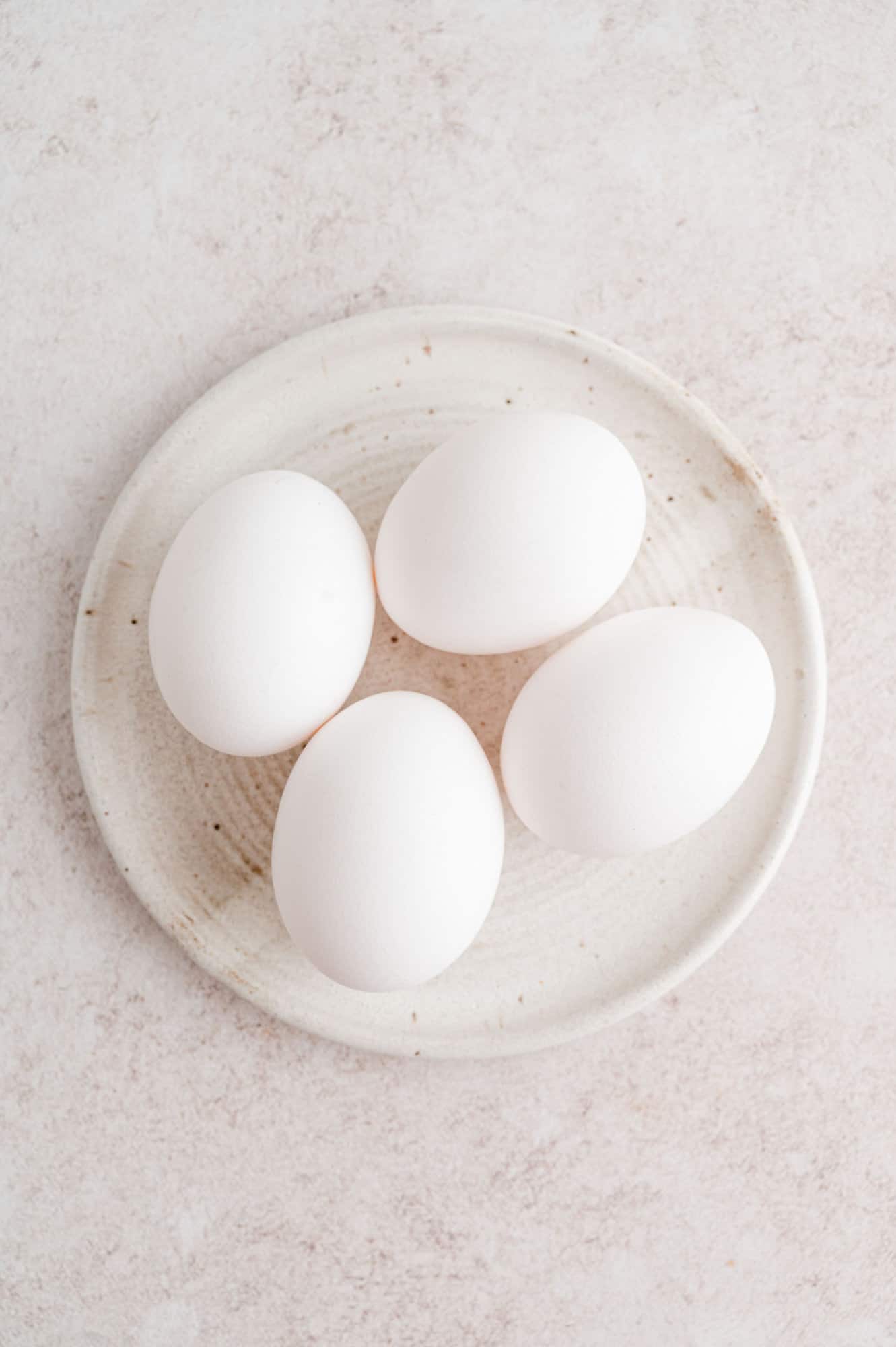 Overhead view of four eggs on a white plate.