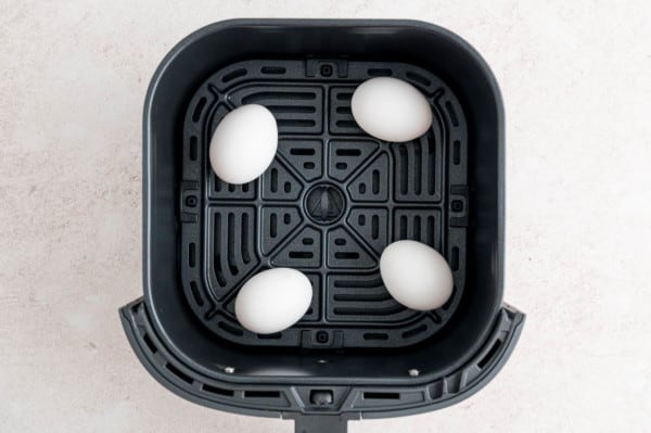 Four eggs arranged inside an air fryer basket.