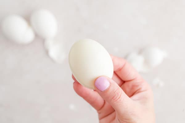 A hand holds up a peeled boiled egg.