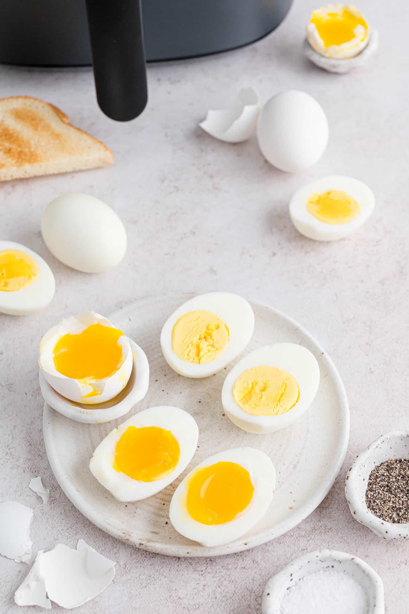 Air fryer boiled eggs cut in half of a plate, surrounded by assorted eggs, toast, and seasoning.