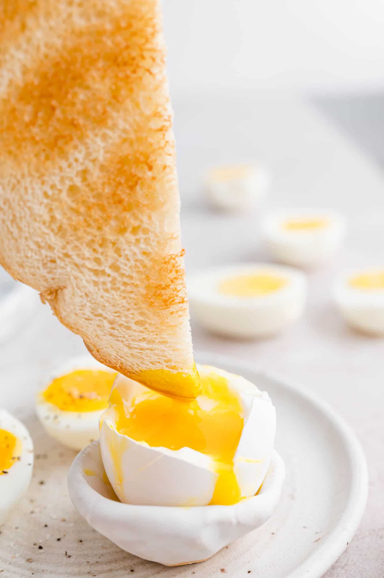 The corner of a piece of toast is dipped into one half of a soft boiled egg on a plate.