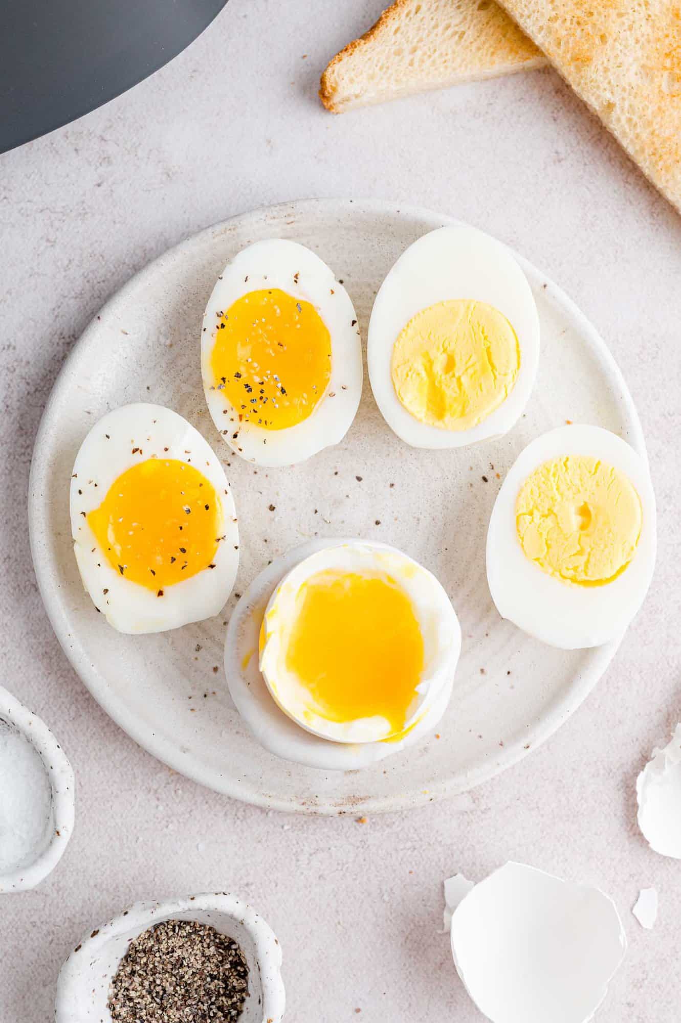 The air fryer is the best way to “boil” eggs that come out perfectly every time! Use this easy method for jammy, soft, or hard-boiled eggs. Seasoned air fryer boiled eggs on a plate, cut in half to reveal yolks cooked to varying doneness.