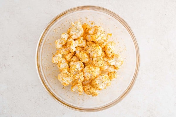 Seasoned cauliflower florets in a glass bowl.