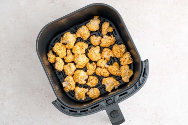 Seasoned uncooked cauliflower florets inside the air fryer basket.