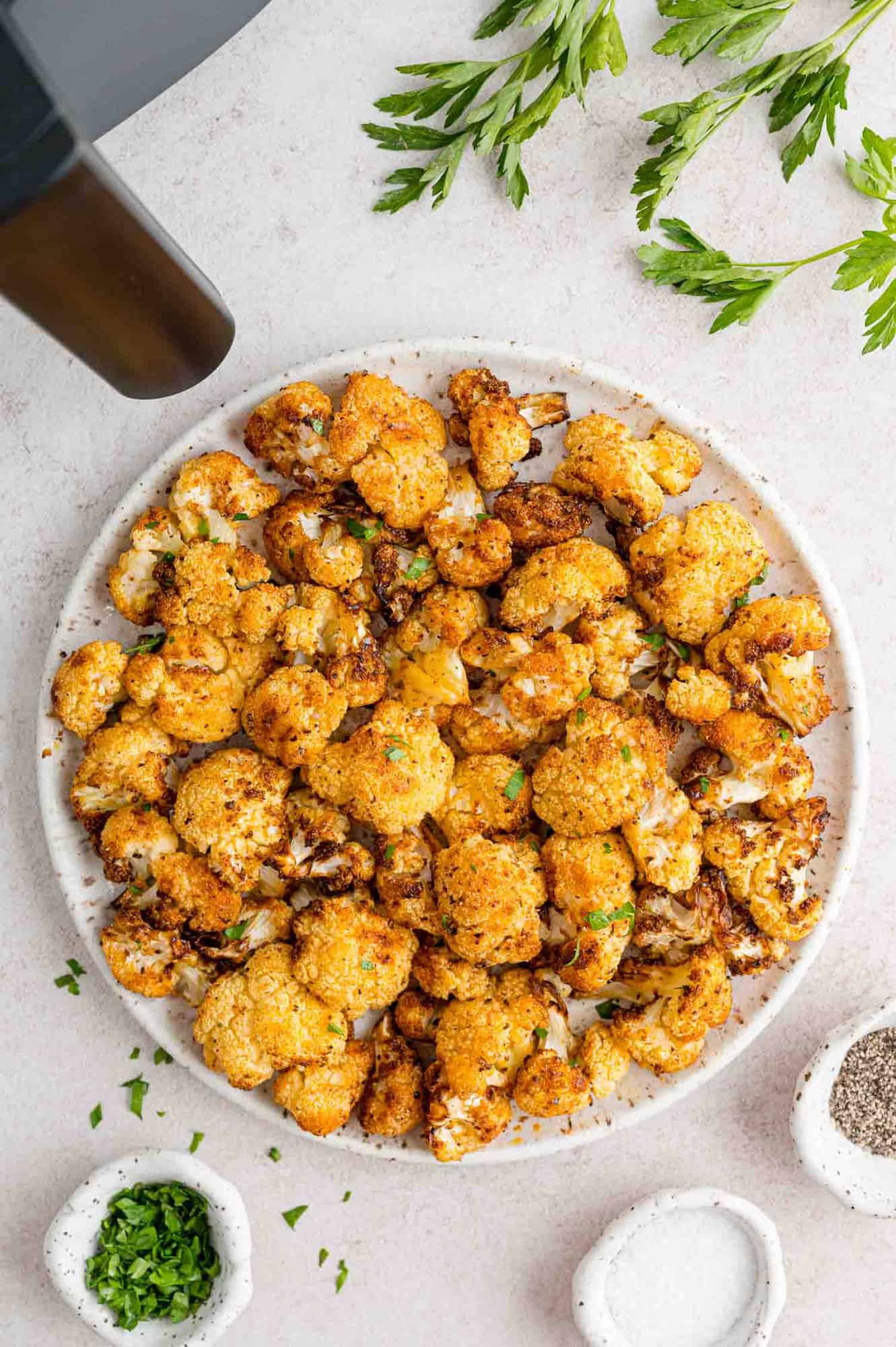 Overhead view of air fried cauliflower on a plate garnished with parsley, next to the air fryer.