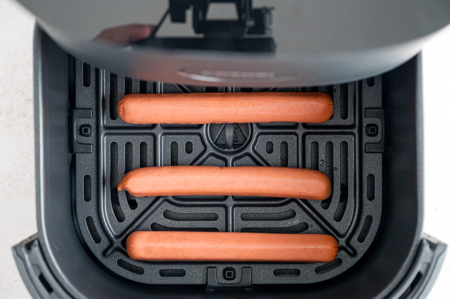 Uncooked hot dogs in air fryer basket.