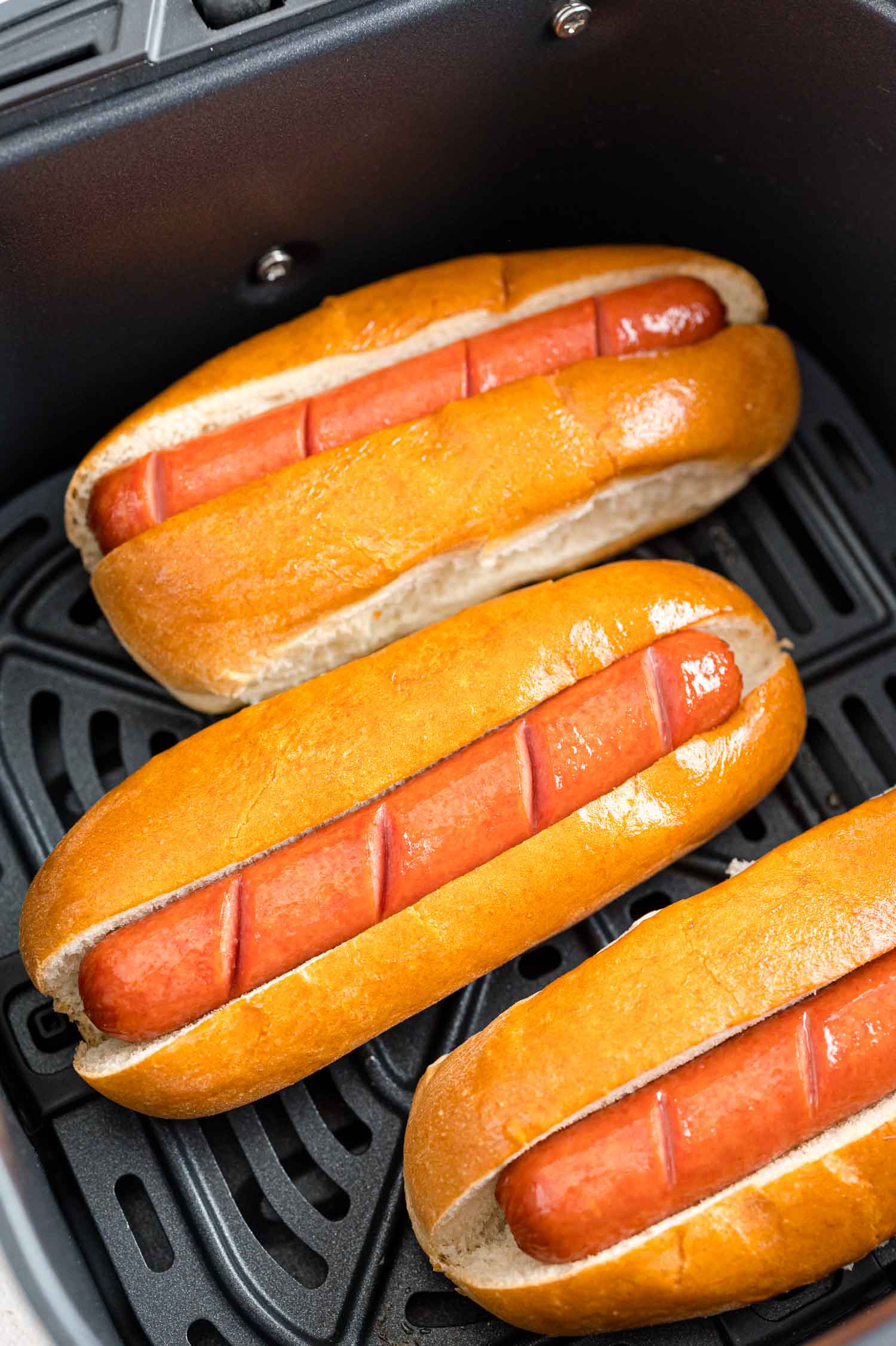 Hot dogs in an air fryer, in buns.