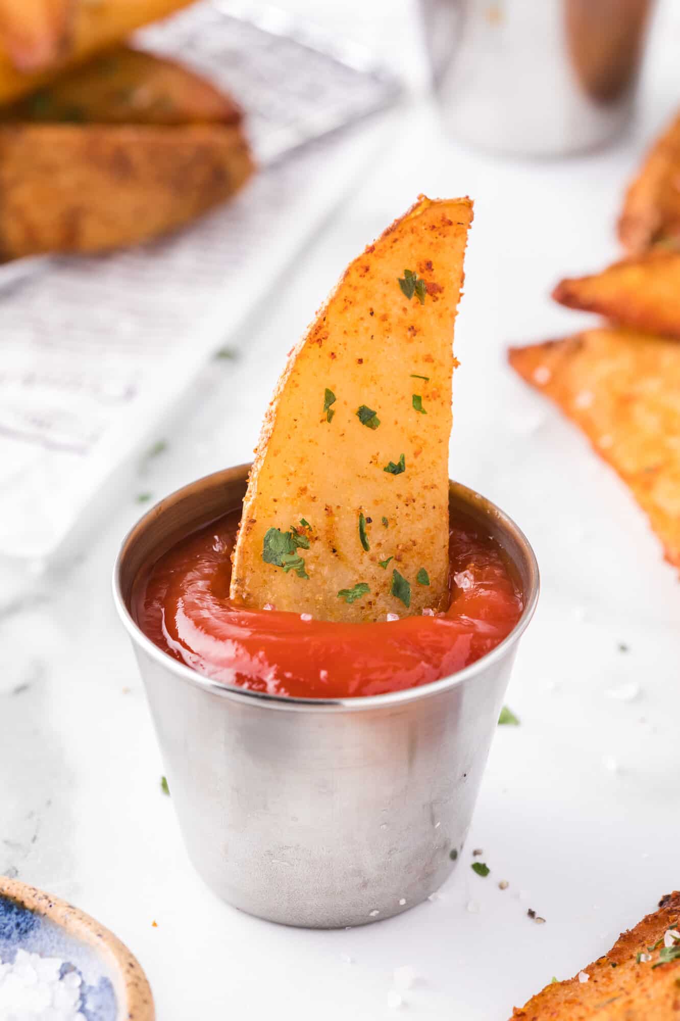 Crispy potato wedge in a small cup of ketchup.