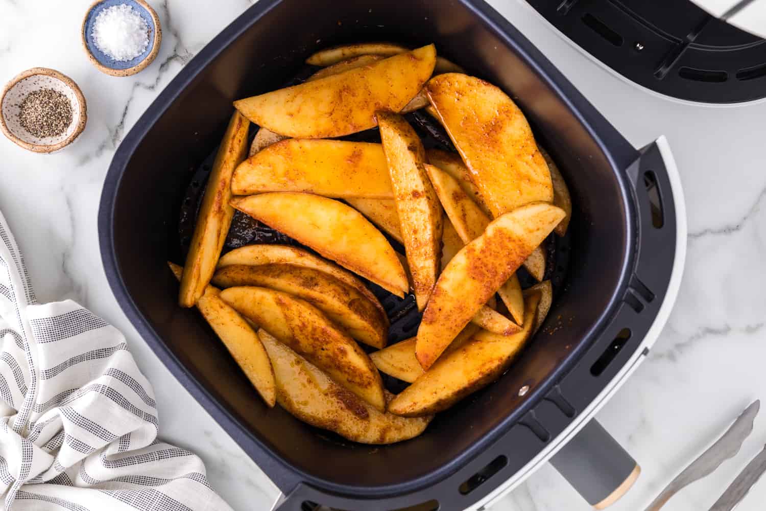 Uncooked potato wedges in air fryer basket.