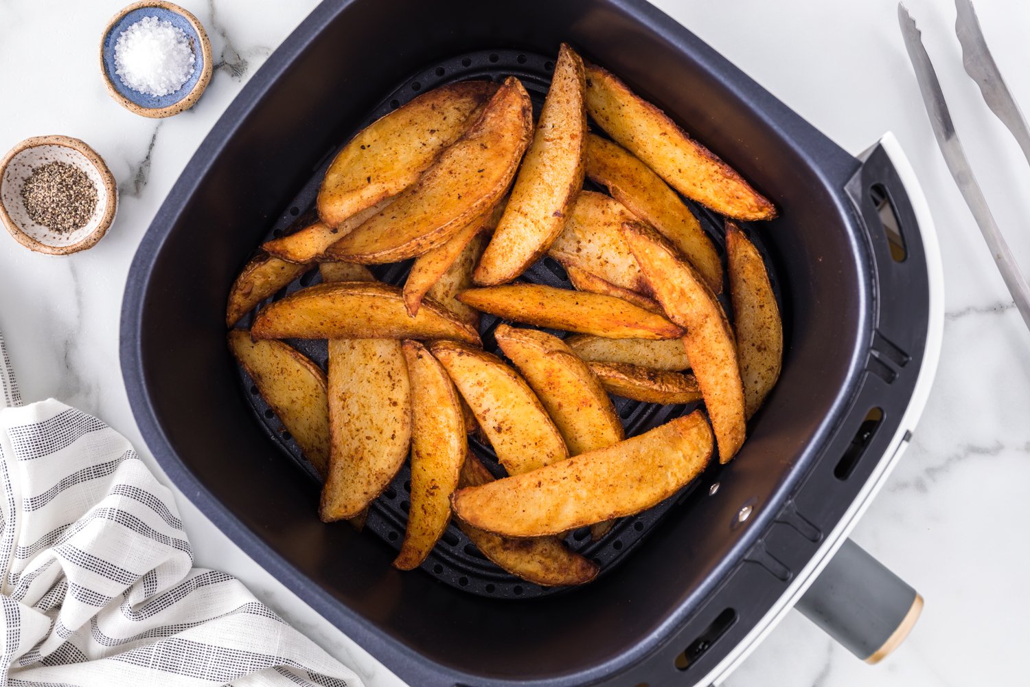 Cooked potato wedges in an air fryer basket.