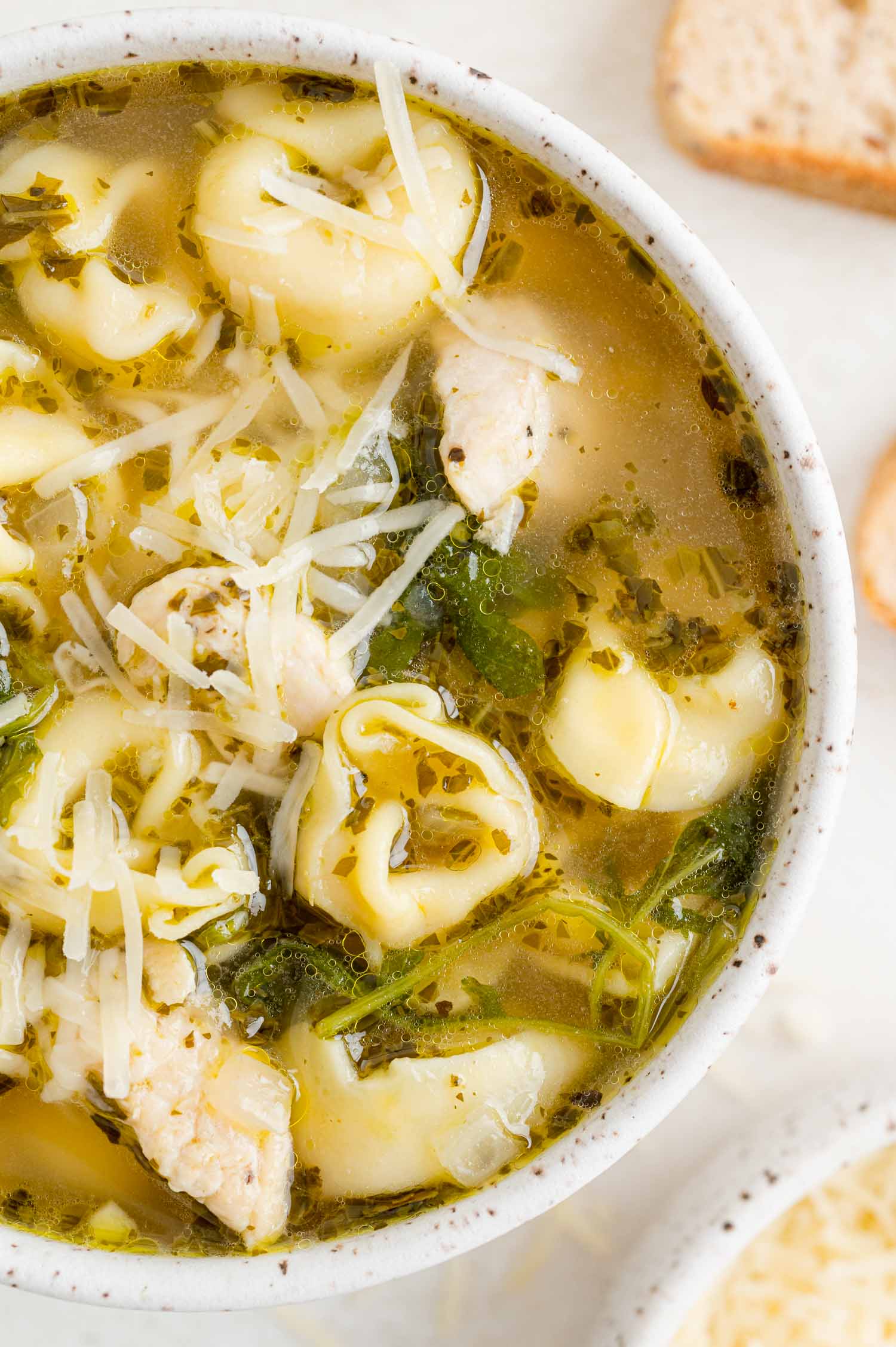 Chicken soup with kale, pesto, tortellini, in a white bowl.