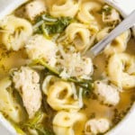 Chicken tortellini soup with kale and pesto, toped with cheese.