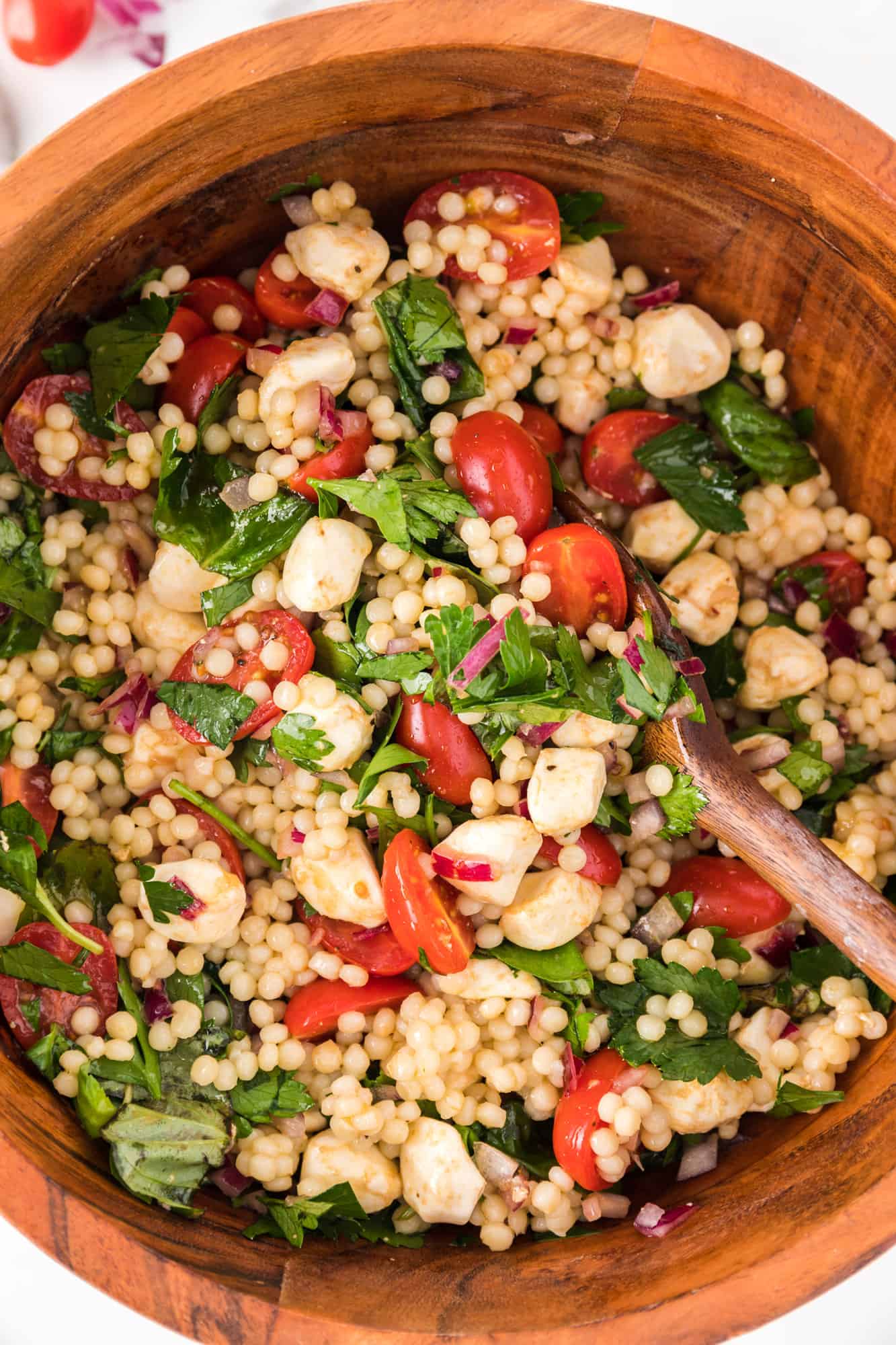 Couscous salad with herbs, tomatoes, mozzarella, in a large wooden bowl.