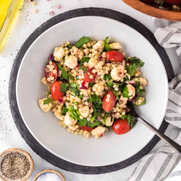 Israeli couscous salad with herbs and tomatoes in a large white bowl.