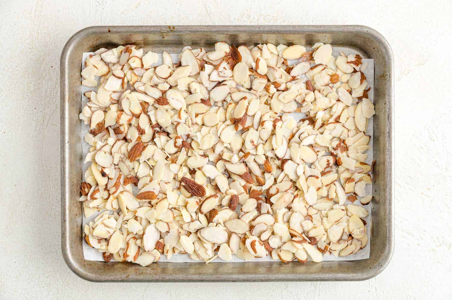 Sliced almonds spread into an even layer on a parchment-lined baking sheet.