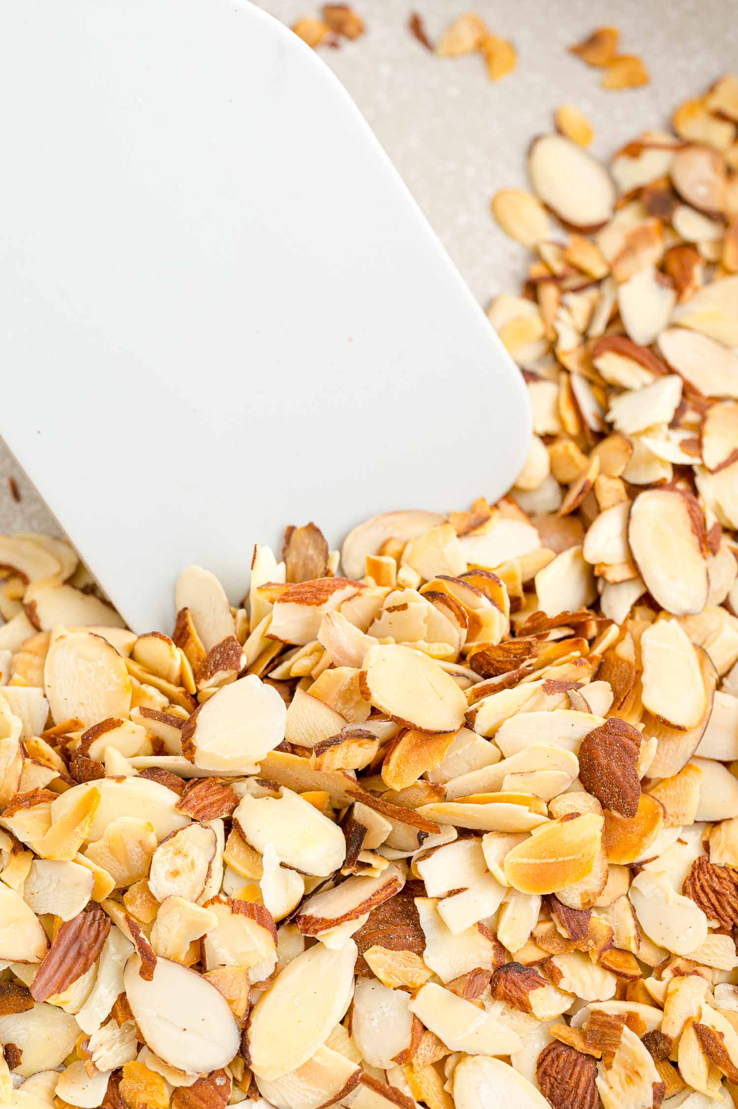 Close up of a spatula stirring almonds as they toast in a skillet.