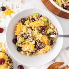 Quinoa salad with orange and grapes in a white bowl.