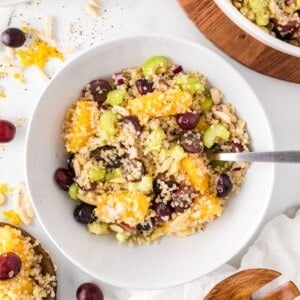 Quinoa salad with orange and grapes in a white bowl.