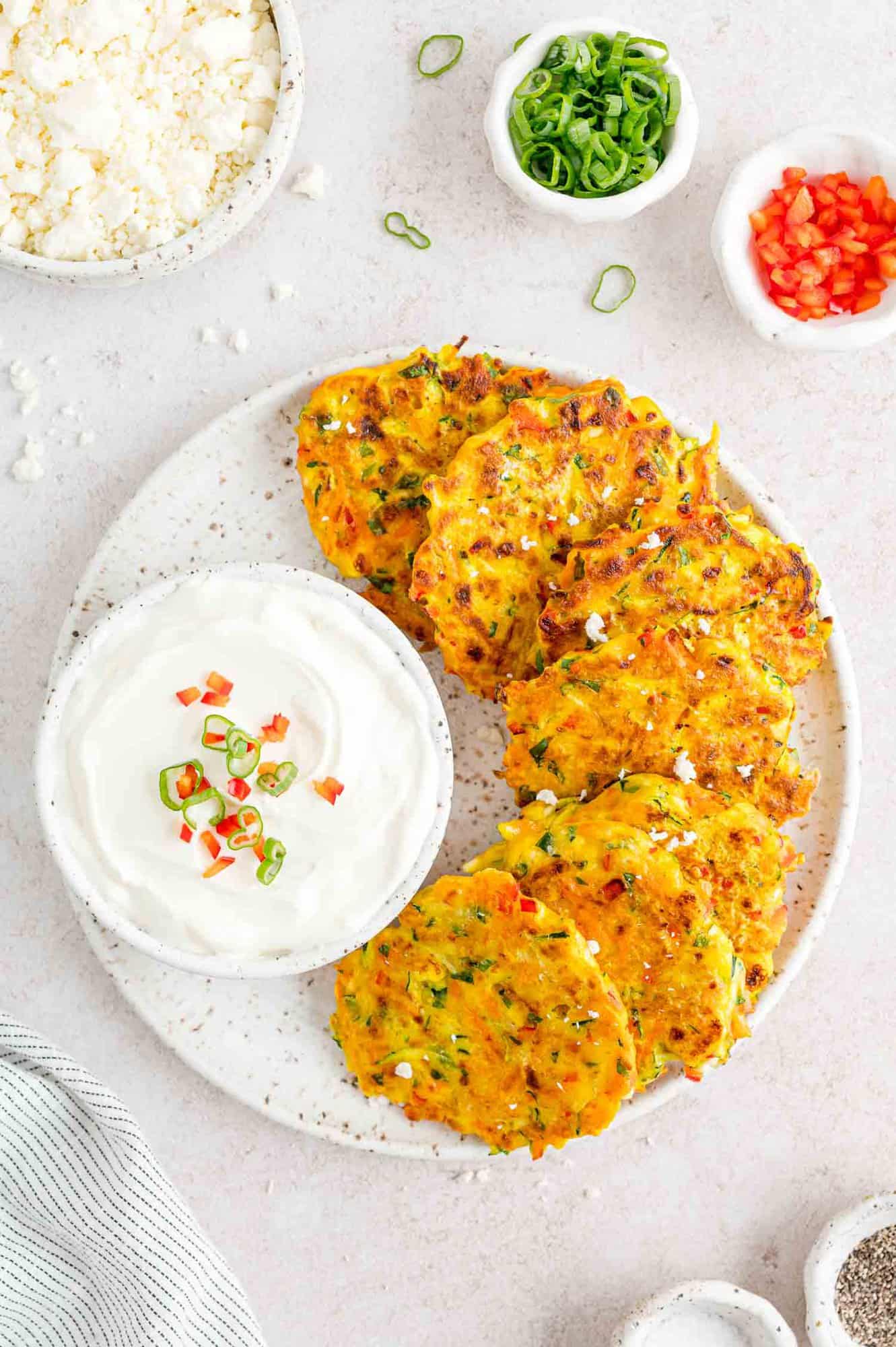 Vegetable fritters on a plate with a bowl of sour cream.