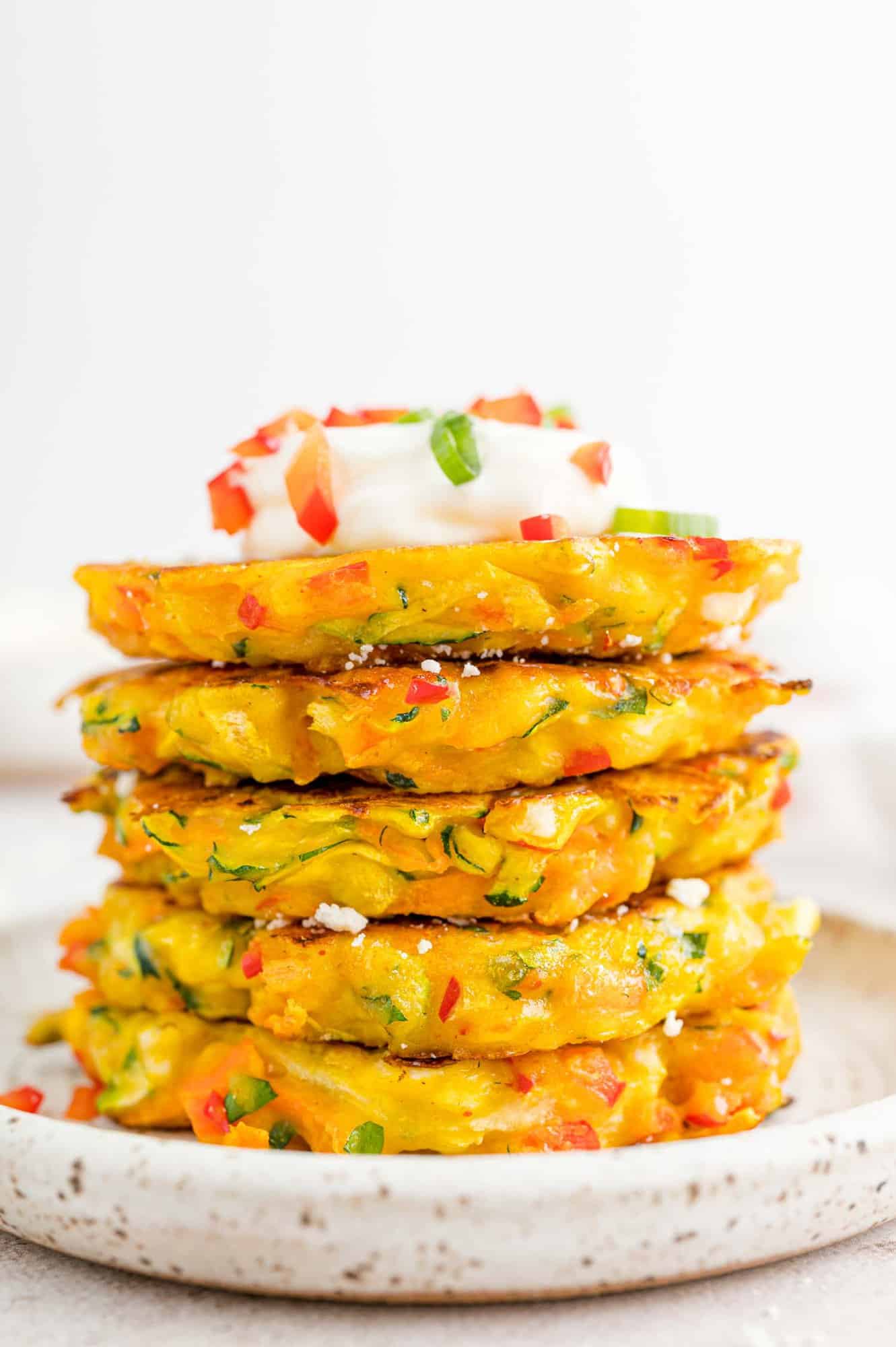 Vegetable fritters stacked in a tall stack topped with sour cream.