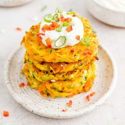 Vegetable fritters stacked in a tall stack topped with sour cream.