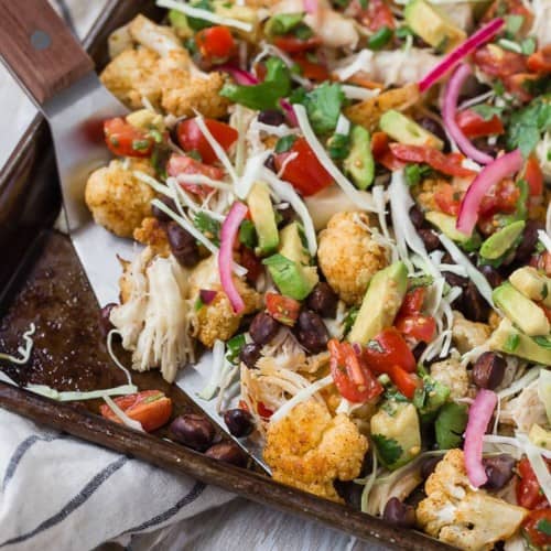 Cauliflower nachos on a sheet pan with colorful toppings.