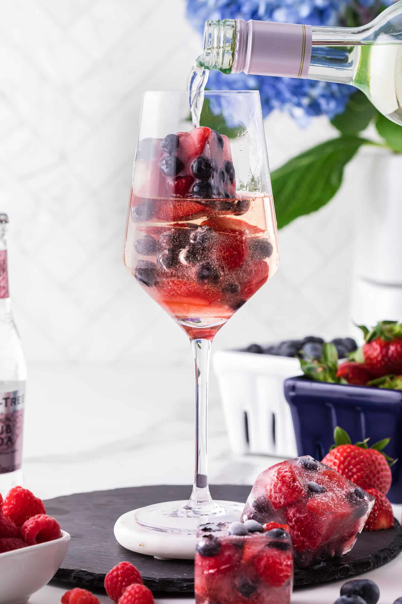 Tall wine glass with white wine spritzer and berry ice cubes.