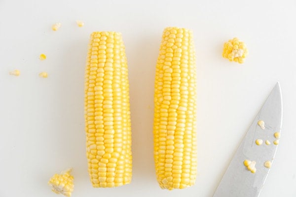 Two ears of corn with the tips trimmed off, next to a sharp knife.