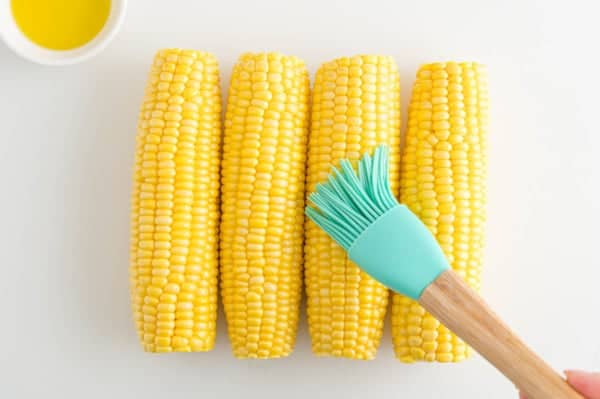 A rubber basting brush is used to brush ears of corn with olive oil.