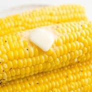 Close up of a pat of butter melting over a stack of air fryer corn on the cob.