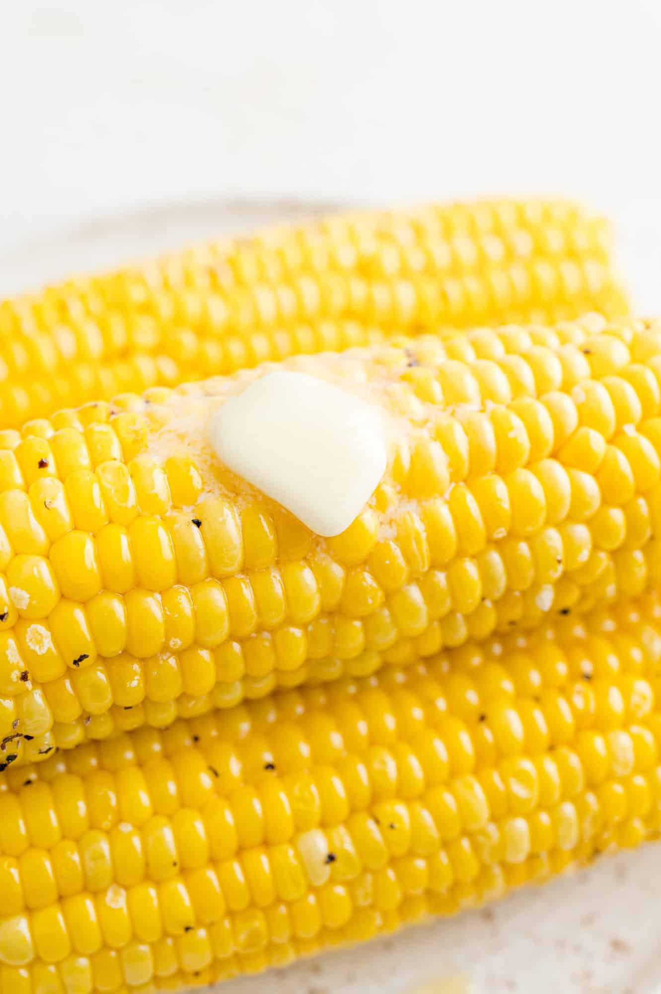 Close up of a pat of butter melting over a stack of air fryer corn on the cob.