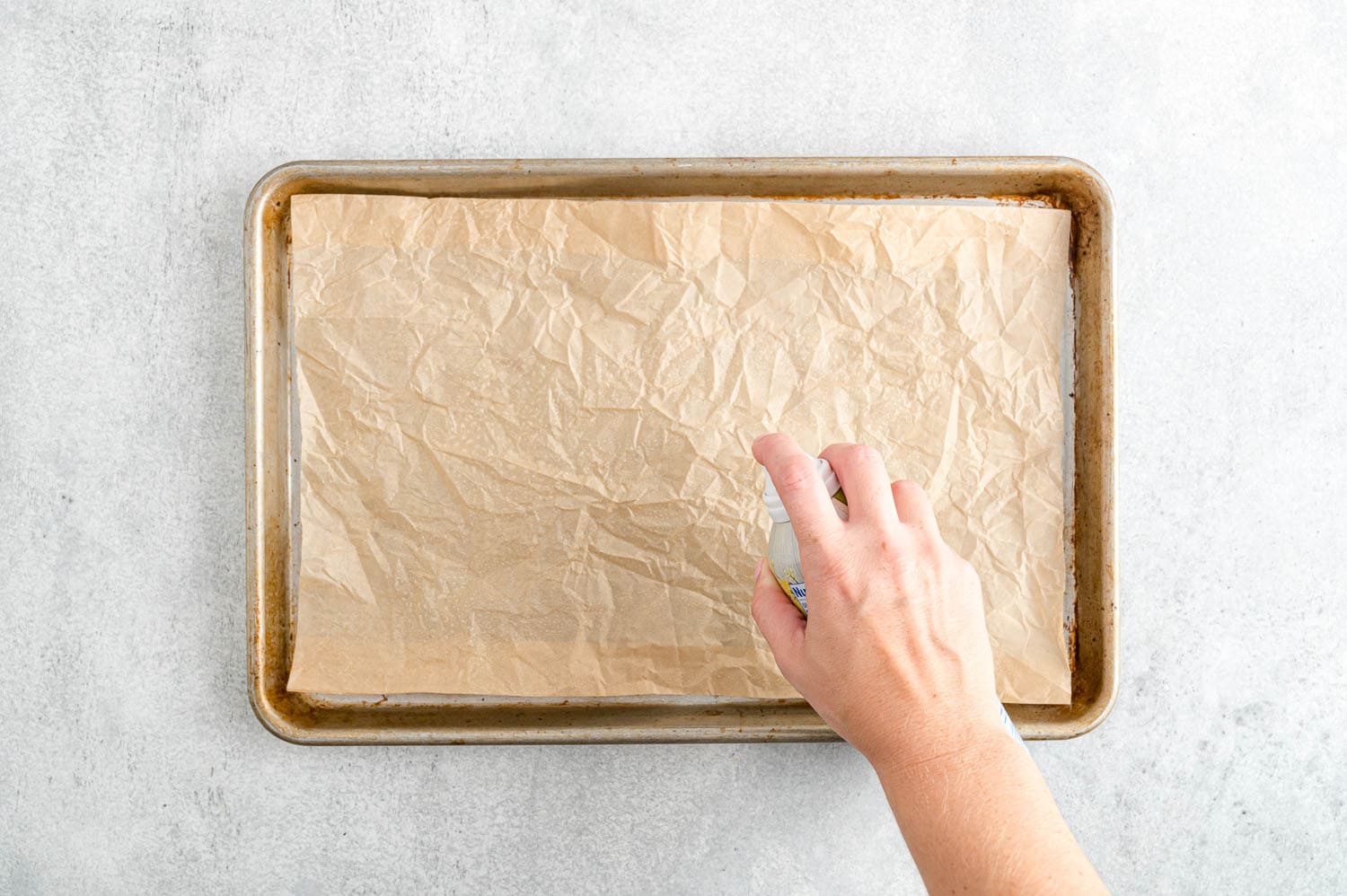 Parchment being sprayed with nonstick spray.