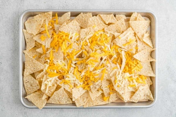 Tortilla chips topped with shredded cheese on a parchment lined baking tray.