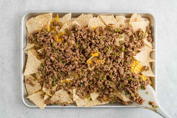 Tortilla chips topped with seasoned taco beef on a parchment lined baking tray.